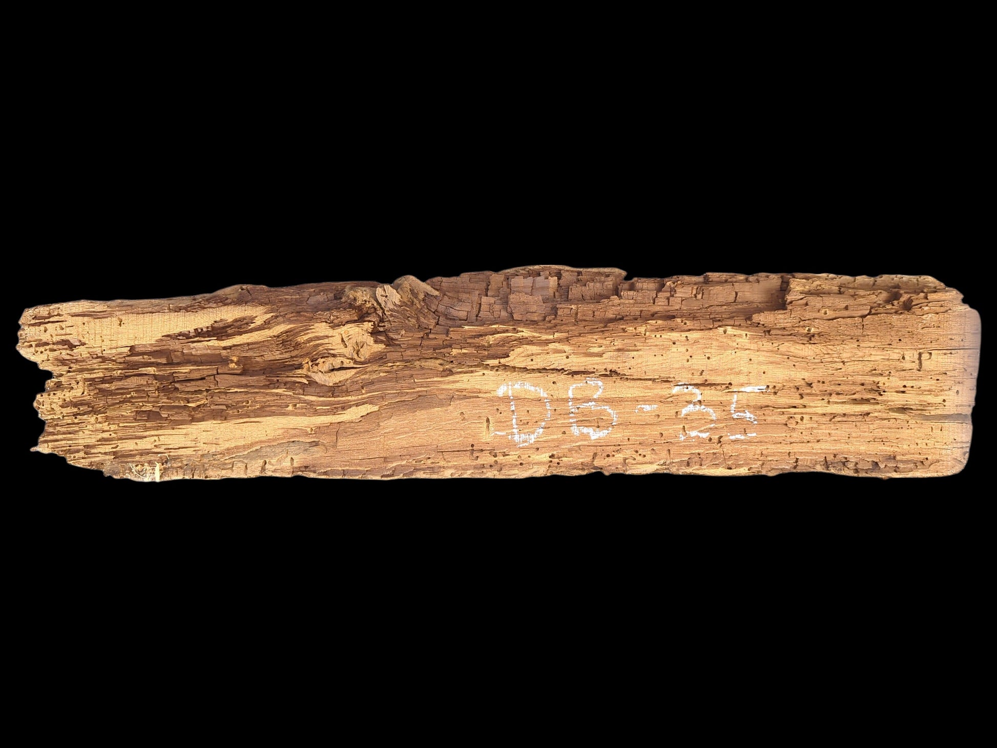 Elongated, light brown reclaimed wood fragment, deeply textured, extensively flaking, crumbly, with many small holes. "DB-35" marked.