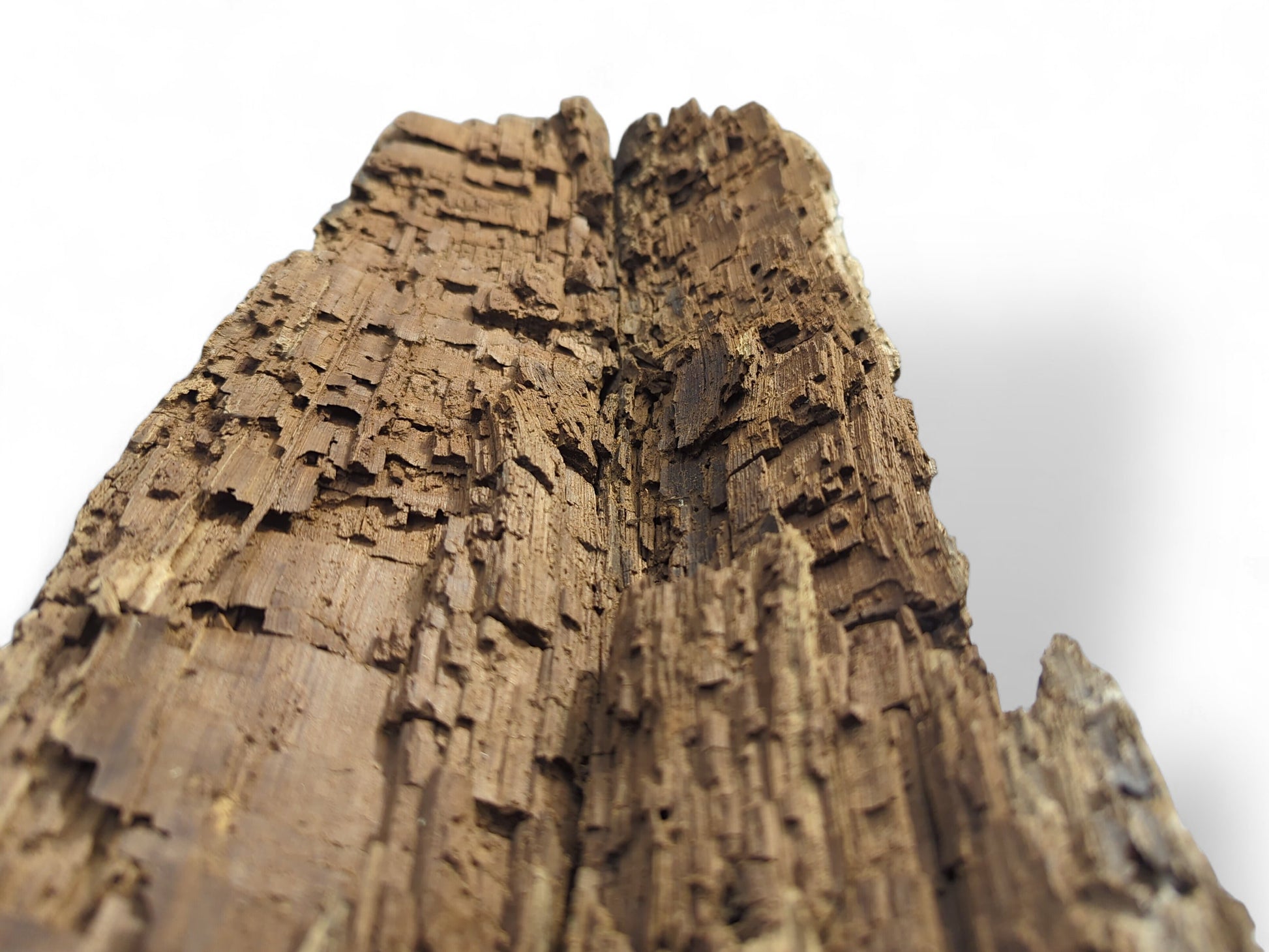 A dark brown, aged reclaimed wood fragment showing deeply textured, fragile, and flaking surfaces.