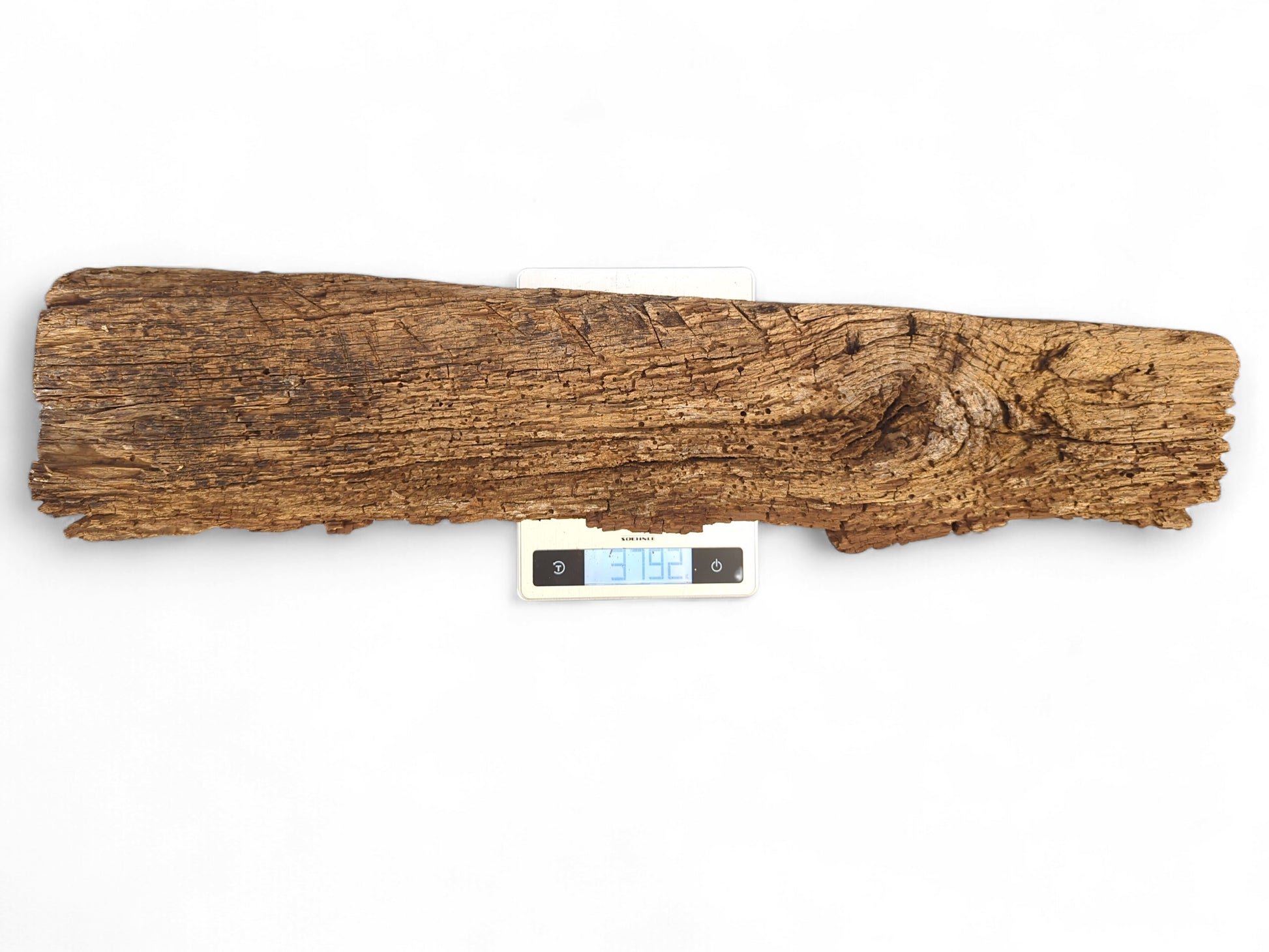 Long, irregular brown wood fragment with rough, flaking surface and visible knot on digital scale.