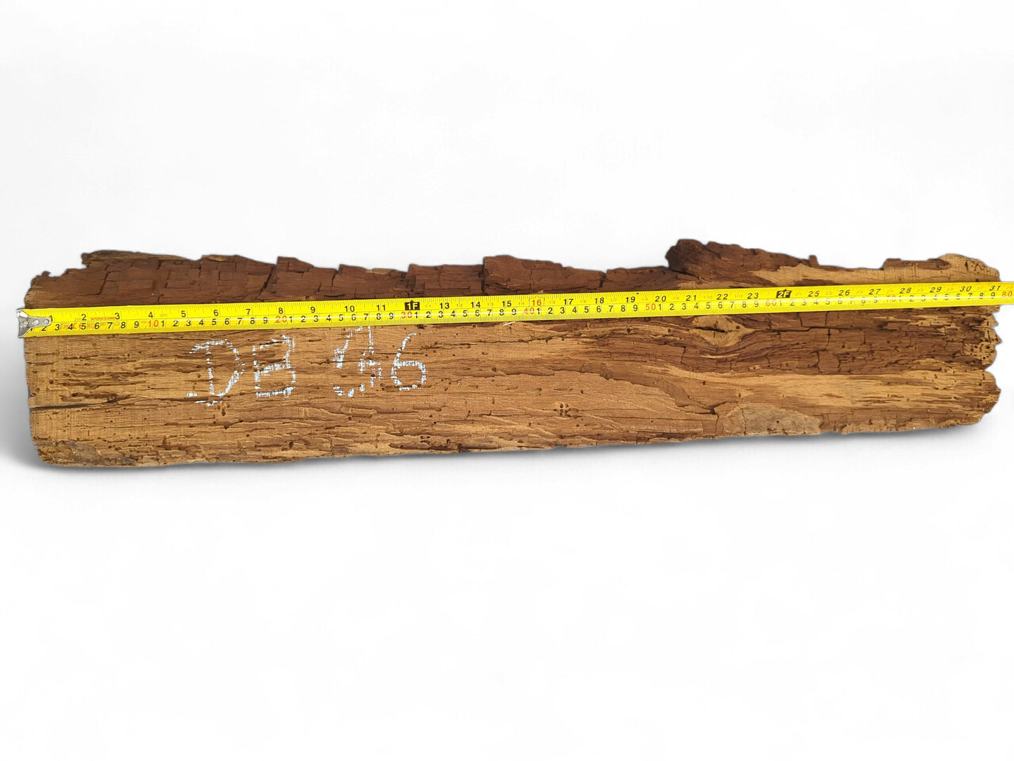 Dark brown, weathered reclaimed wood beam fragment with a fragile, flaking surface and measuring tape.