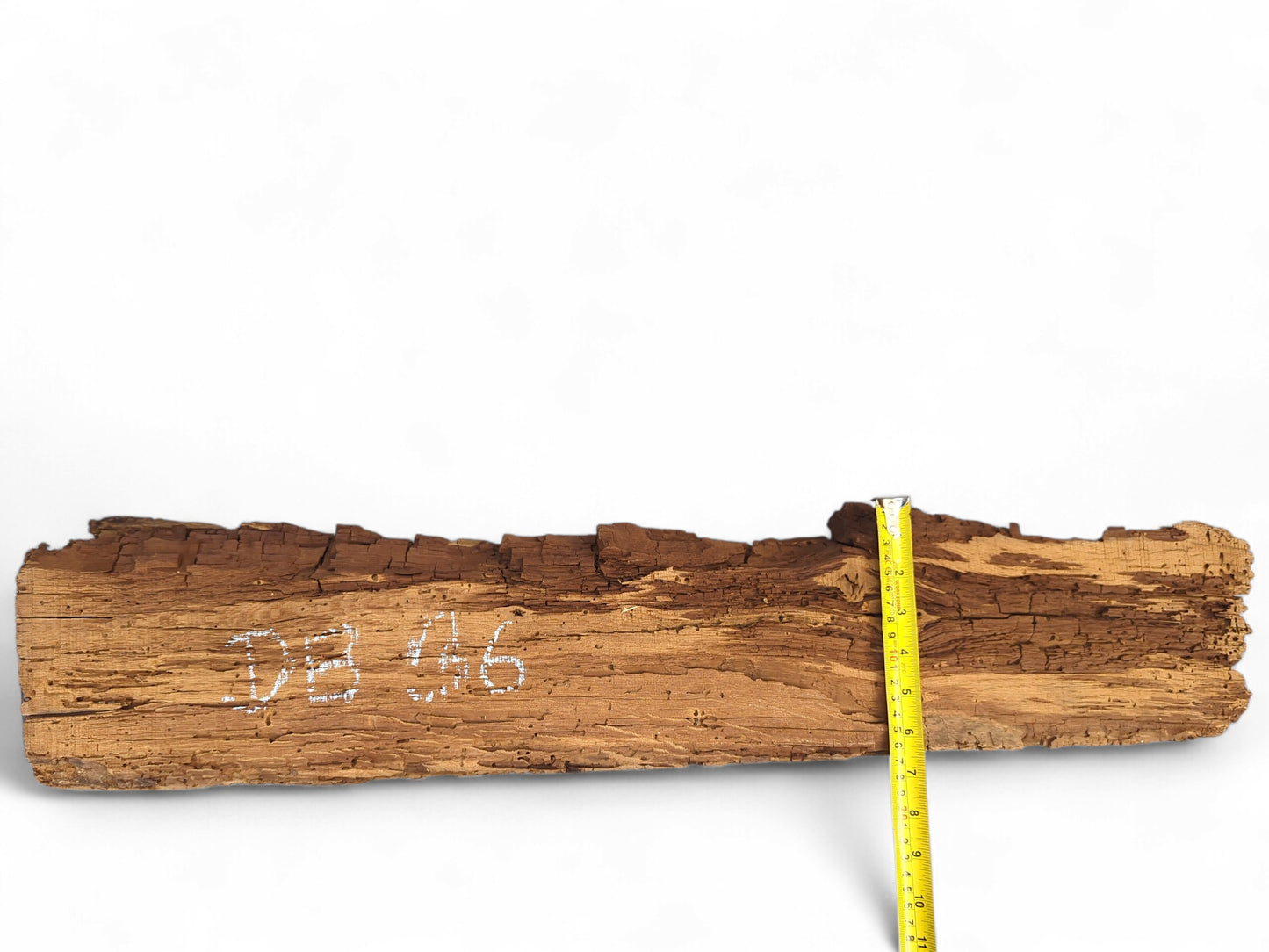 Weathered brown wood beam fragment with severe flaking, white 'DB 036' marking, and a yellow tape measure.
