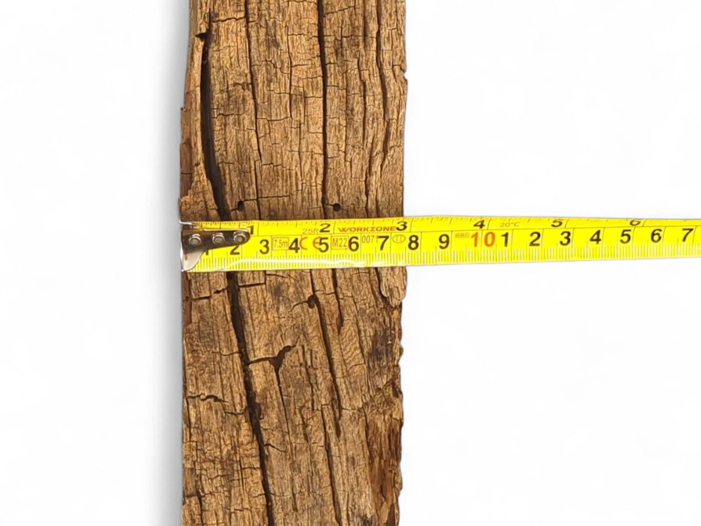 A brown, weathered reclaimed wood beam fragment with deep cracks, rough texture, and yellow tape measure.