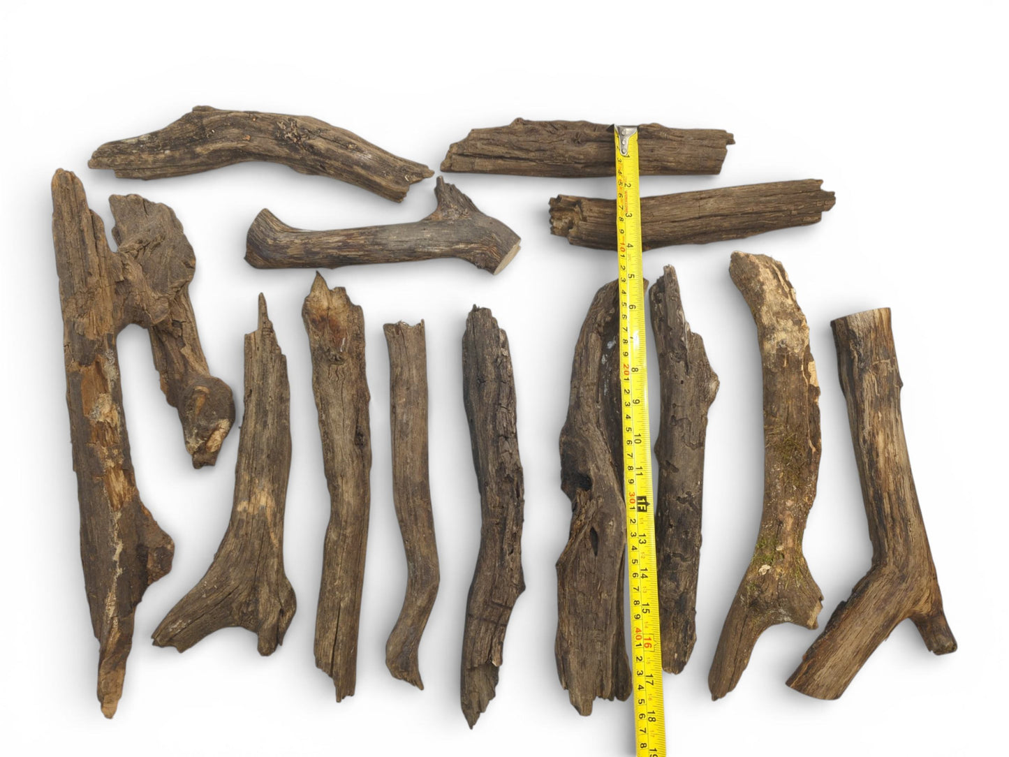A yellow tape measure is laid alongside multiple weathered, brown wood pieces to indicate their size.