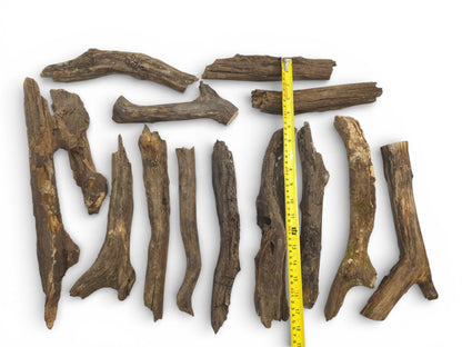A yellow tape measure is laid alongside multiple weathered, brown wood pieces to indicate their size.