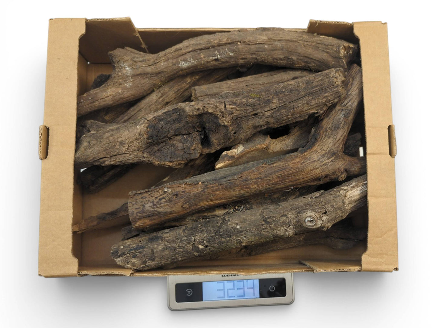 A cardboard box of weathered, barkless wood branches sits on a digital scale showing the total weight.