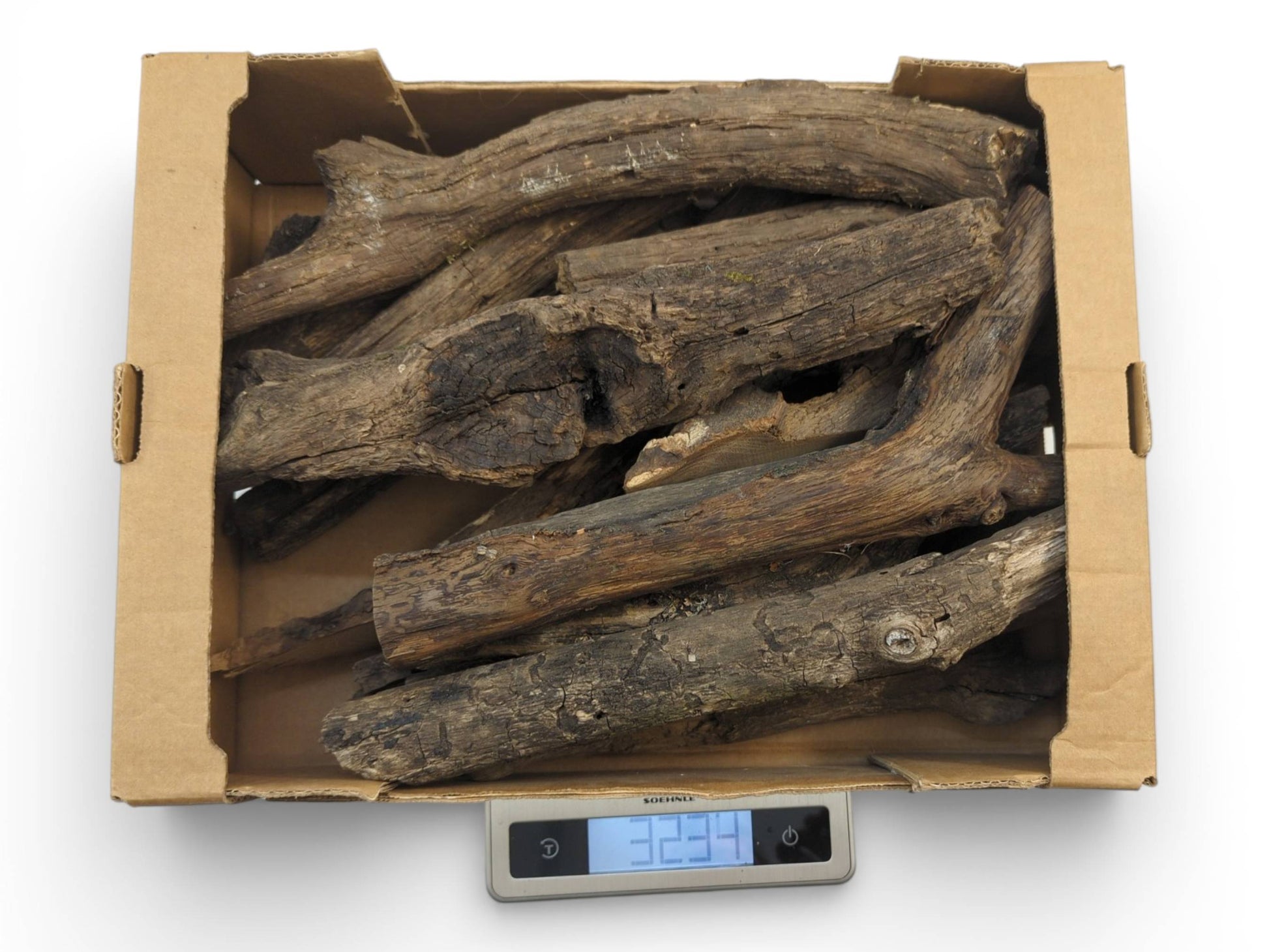 A cardboard box of weathered, barkless wood branches sits on a digital scale showing the total weight.