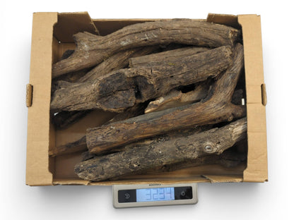 A cardboard box of weathered, barkless wood branches sits on a digital scale showing the total weight.