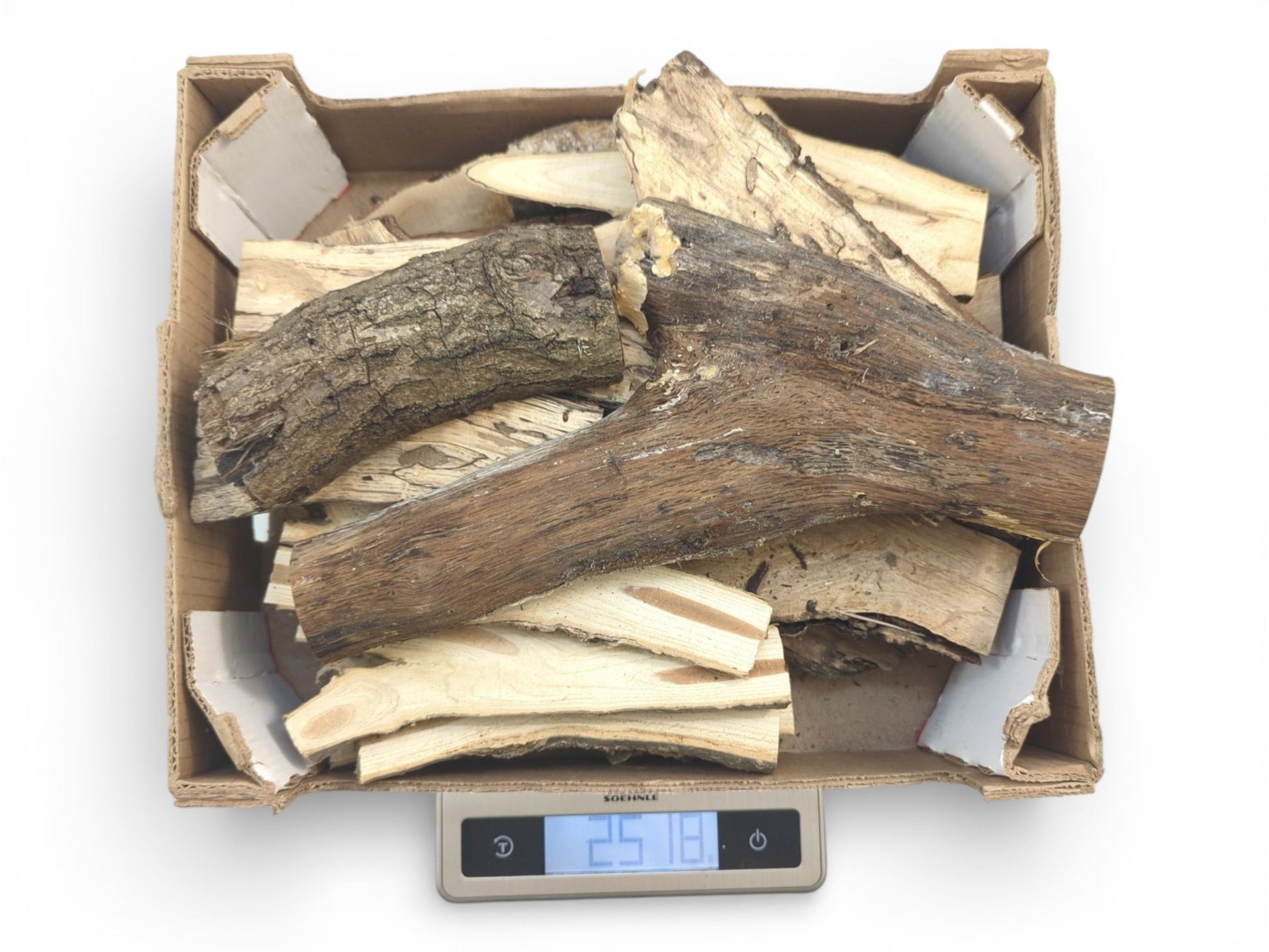 A cardboard box filled with various split wood pieces with bark is weighed on a digital scale.