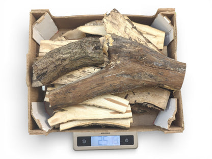 A cardboard box filled with various split wood pieces with bark is weighed on a digital scale.