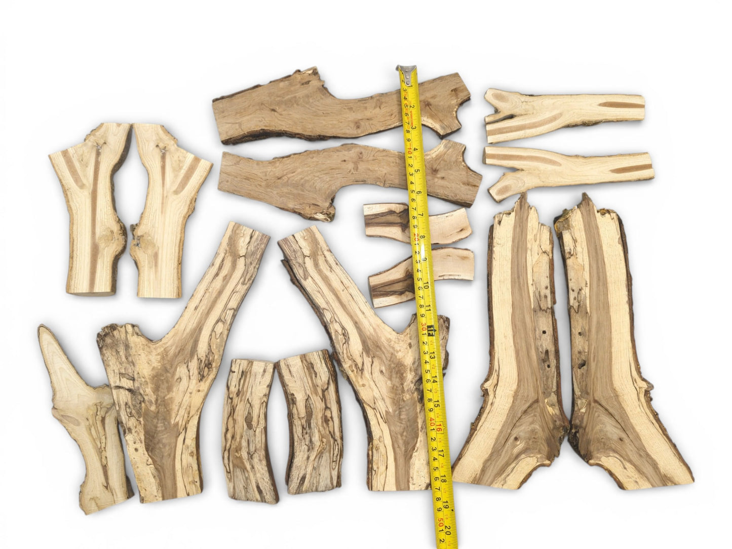 An assortment of split wood branches with varied grain patterns arranged by a yellow tape measure.