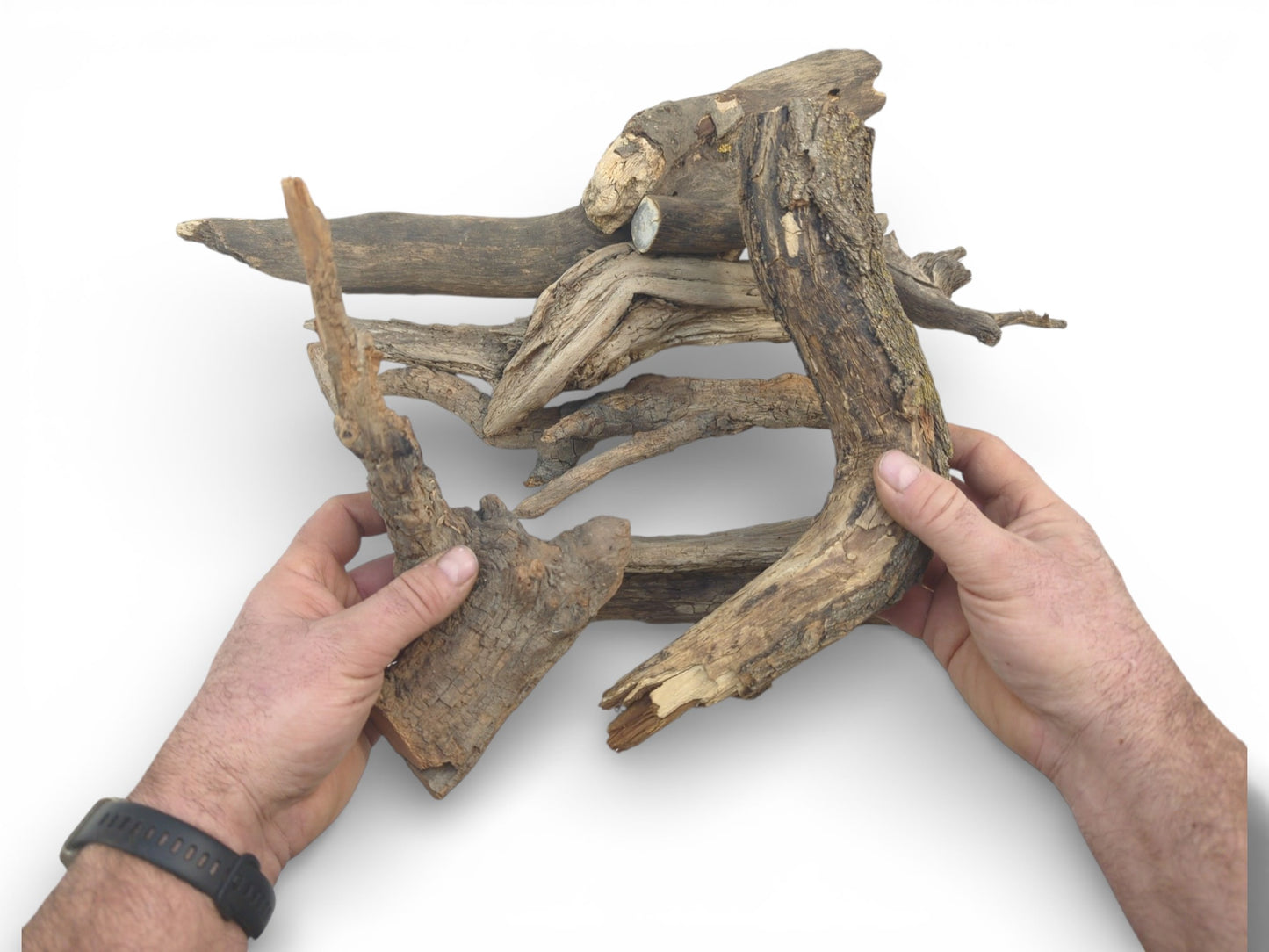 A top-down shot of hands arranging a collection of gnarled, bark-covered wood pieces into a composition.