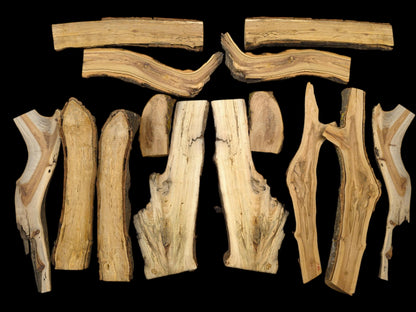 A flat lay of split forest branches with varied grains and bark edges on a black surface.