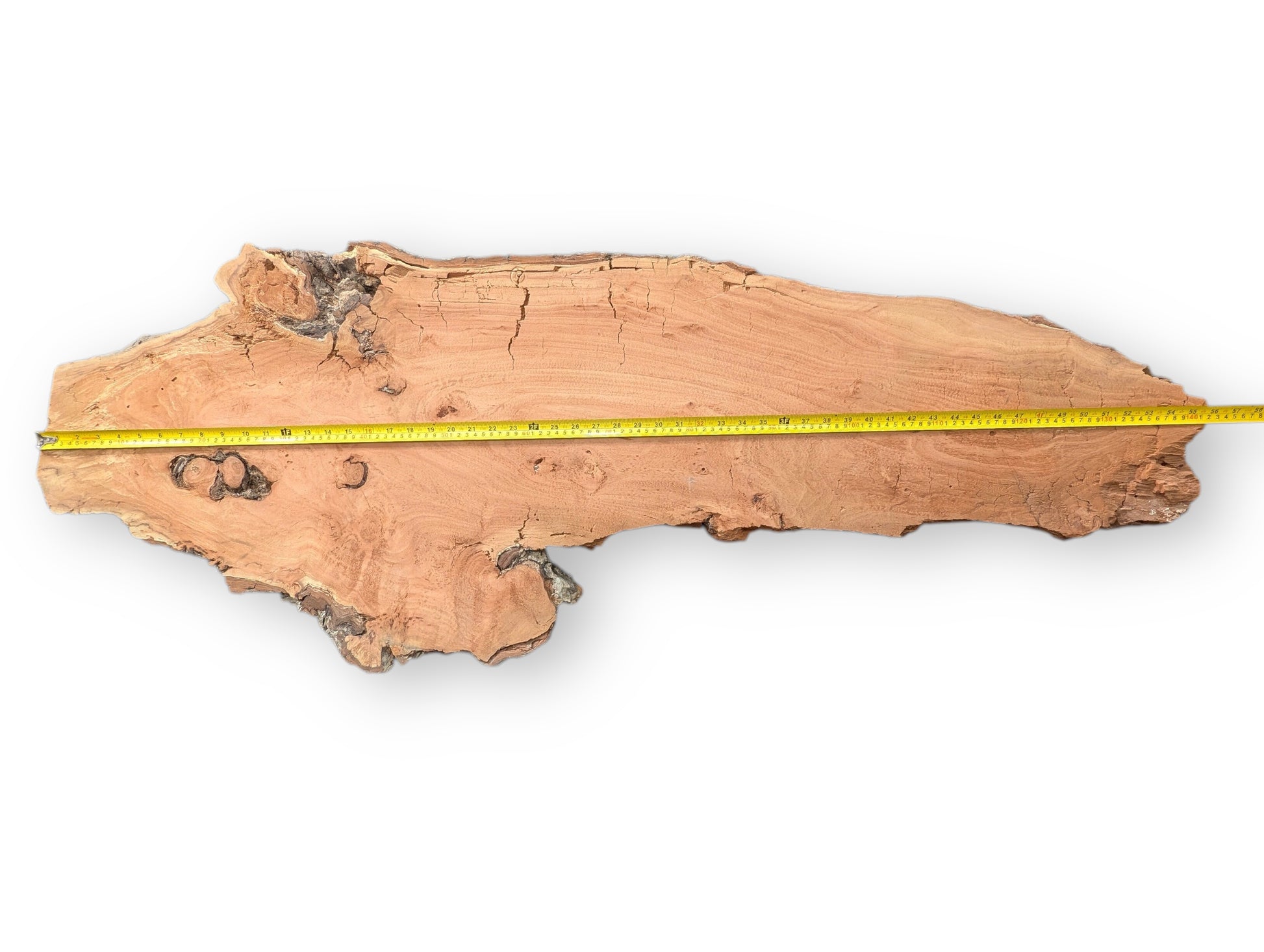 Measuring tape across an irregular reddish-brown willow wood slab, showing grain and extensive surface cracks.