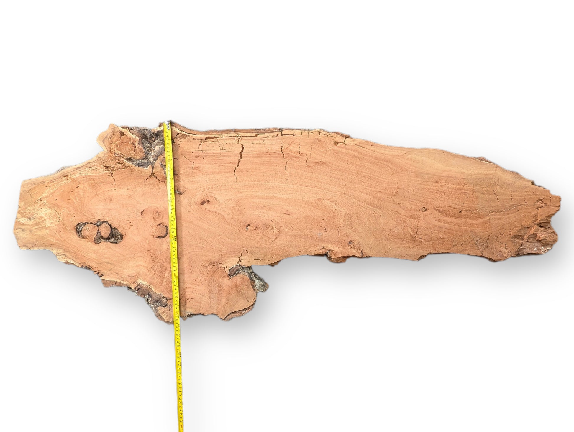 Irregular reddish-brown willow wood slab with extensive cracks, visible grain, natural bark edges, and a vertical measuring tape.