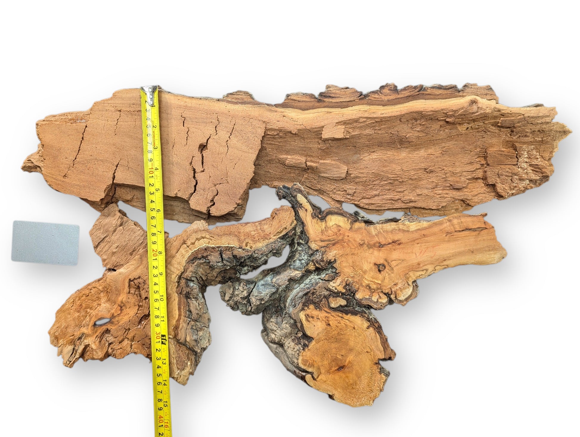 Two irregular, textured brown and grey willow wood pieces, yellow measuring tape, grey block.