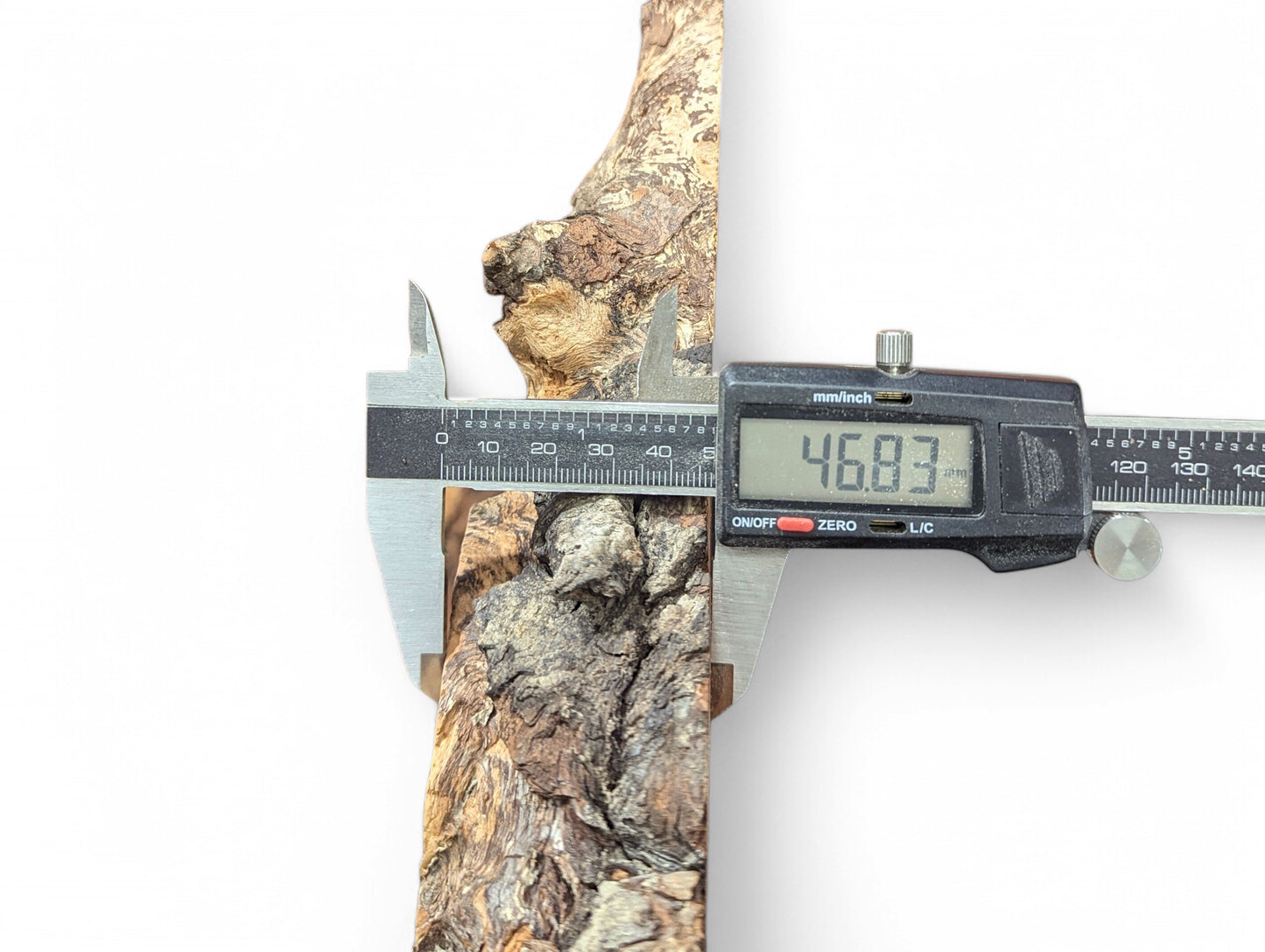 Digital caliper measures a textured, brown and grey wood piece, displaying 46.83 mm on its screen.