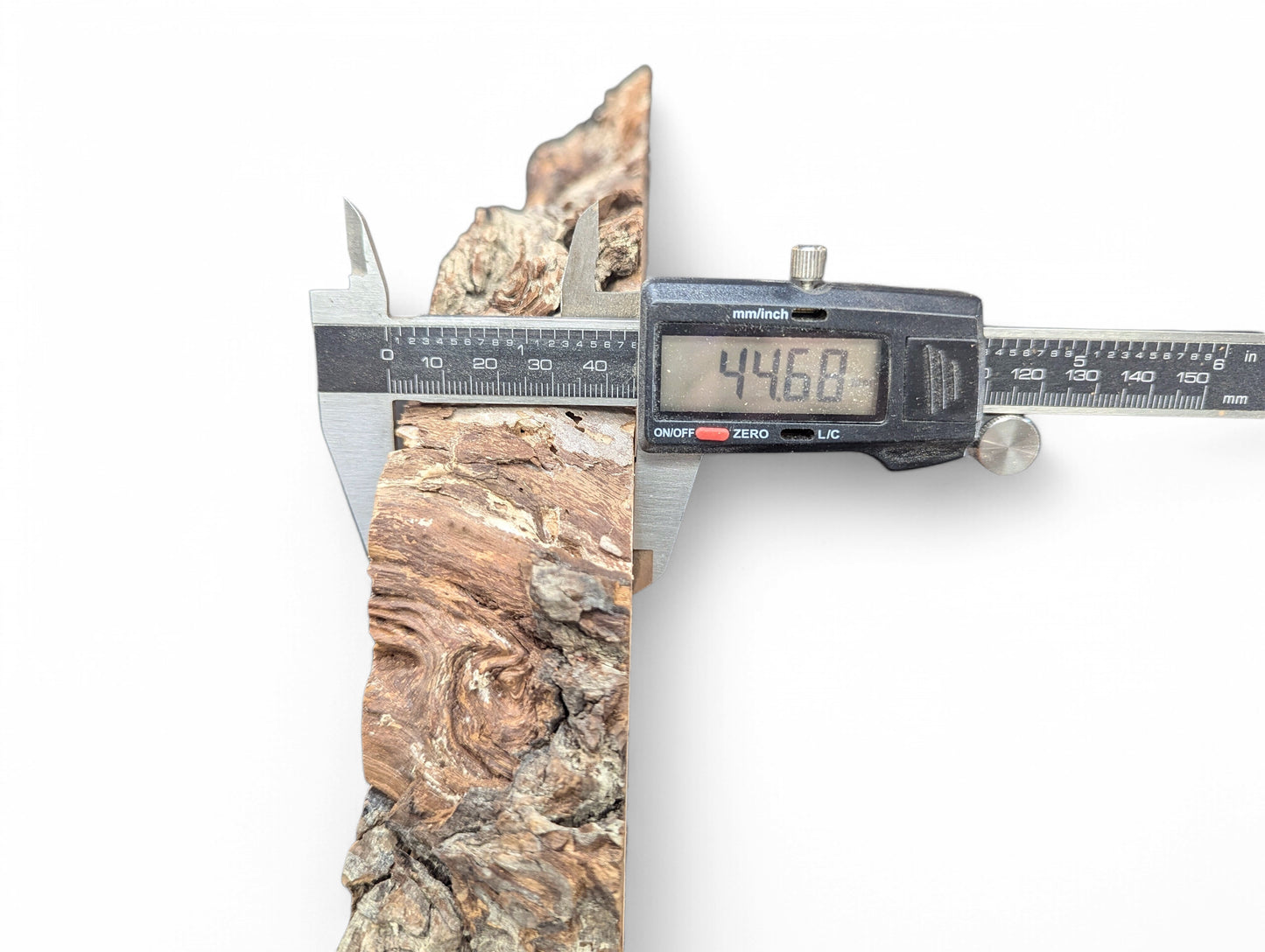 Digital caliper measures an irregular, light brown willow wood slice with cracks and rough texture, showing 44.68mm.