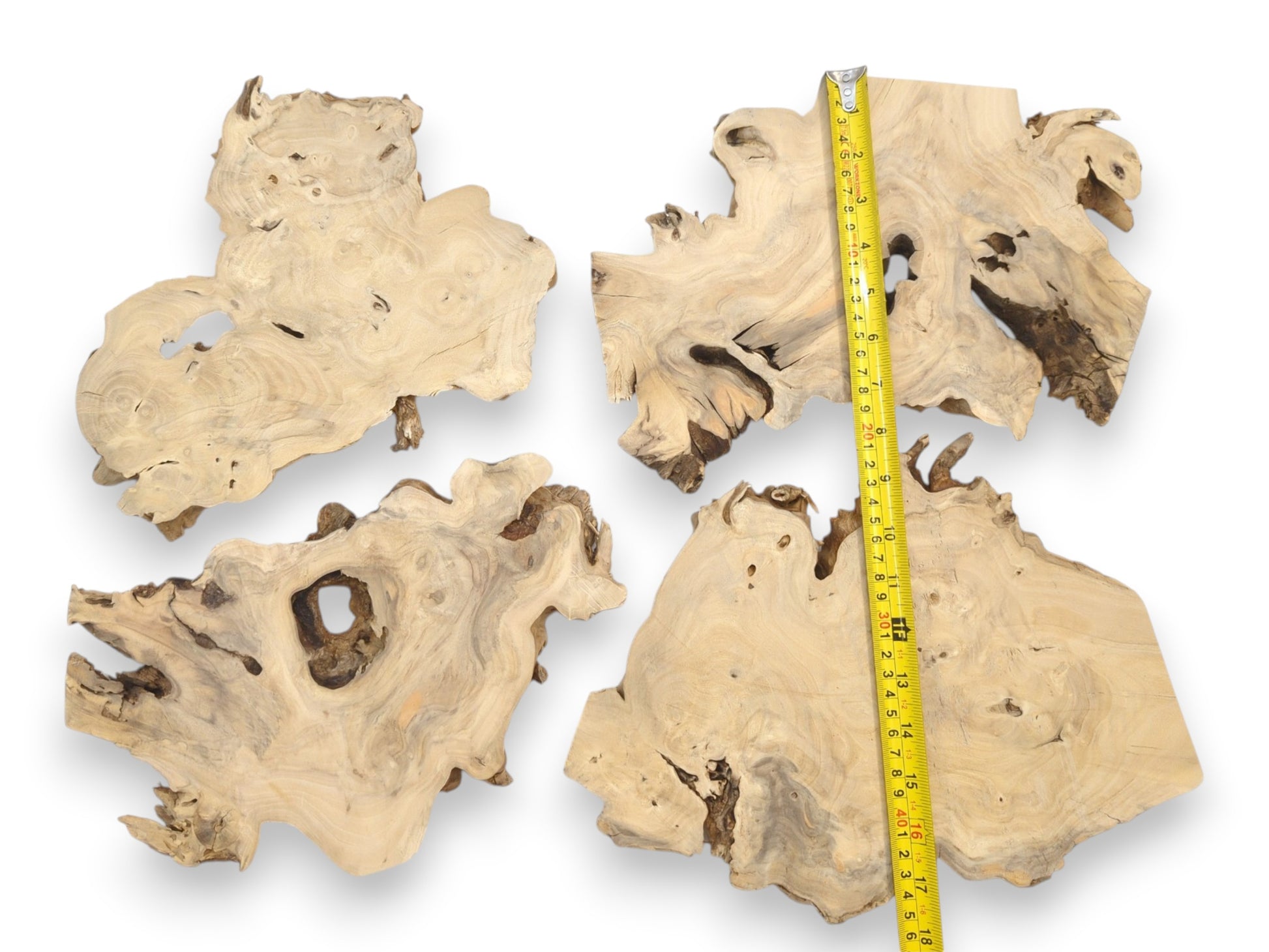 An overhead view of four irregular timber slabs with voids, measured by a tape.
