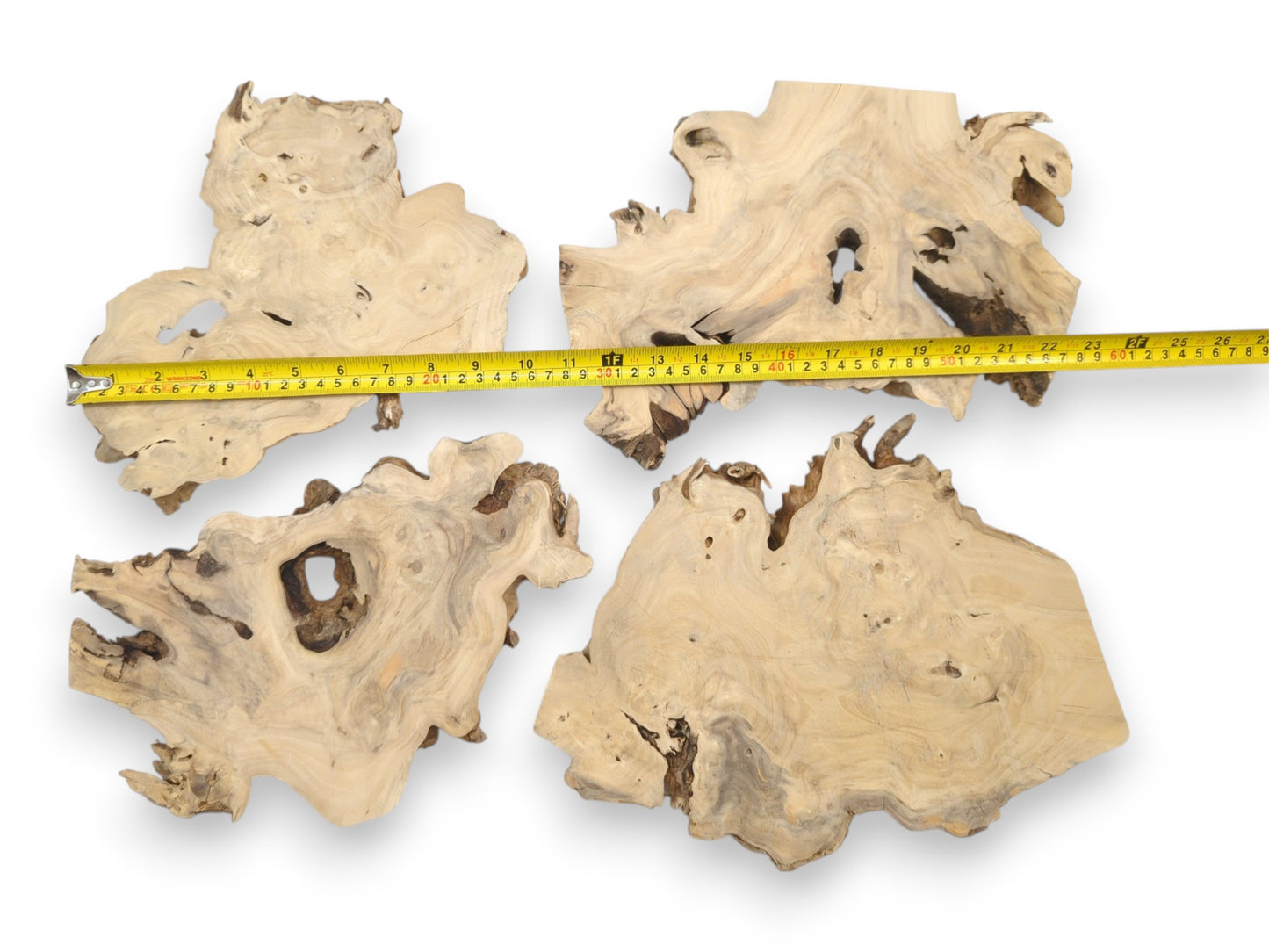 A yellow tape measure stretches across four irregular, light-toned timber slabs with natural voids.