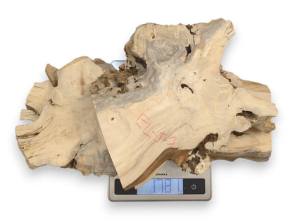 A digital scale weighs four stacked, pale wood slabs with rugged bark and red marks.