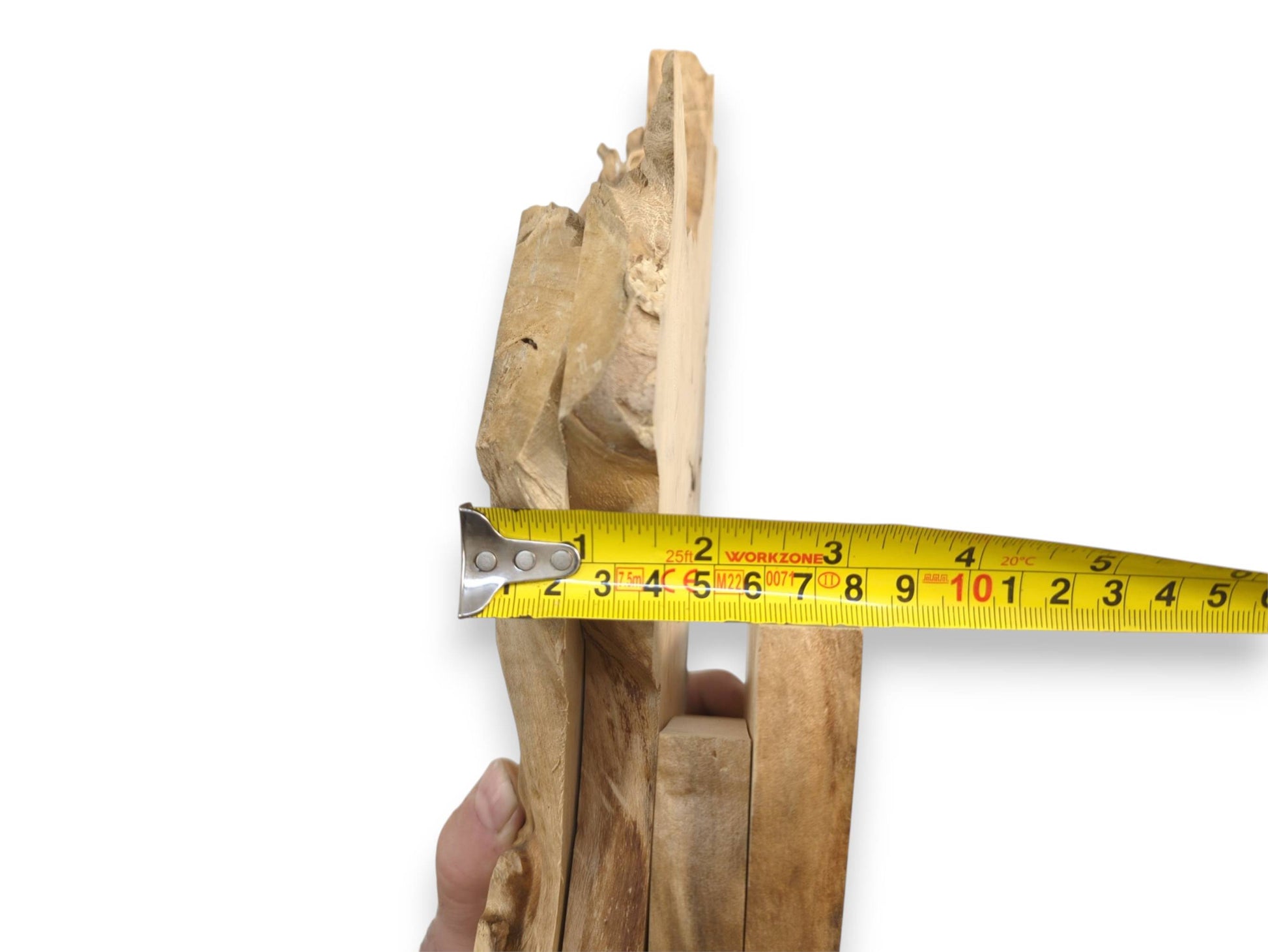 A hand grips four stacked wood sections while a tape measure gauges their total width.