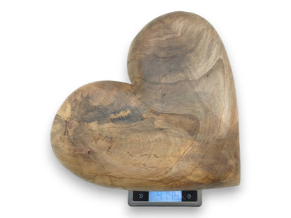 A carved wooden heart with dark mineral streaks and end grain rests on a digital scale.