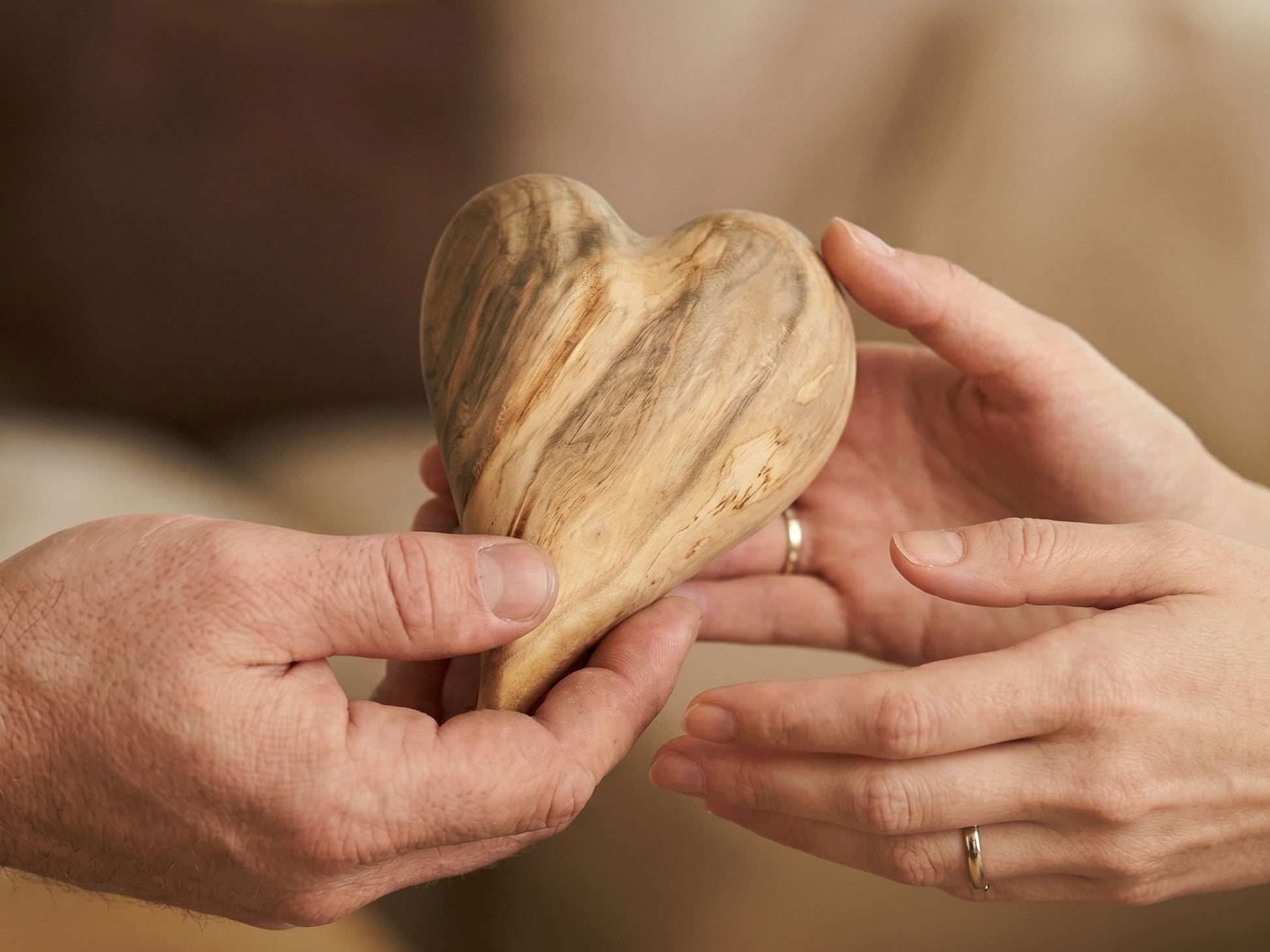 A close-up shows a heart-shaped timber with dramatic, wavy grain passed between two hands.