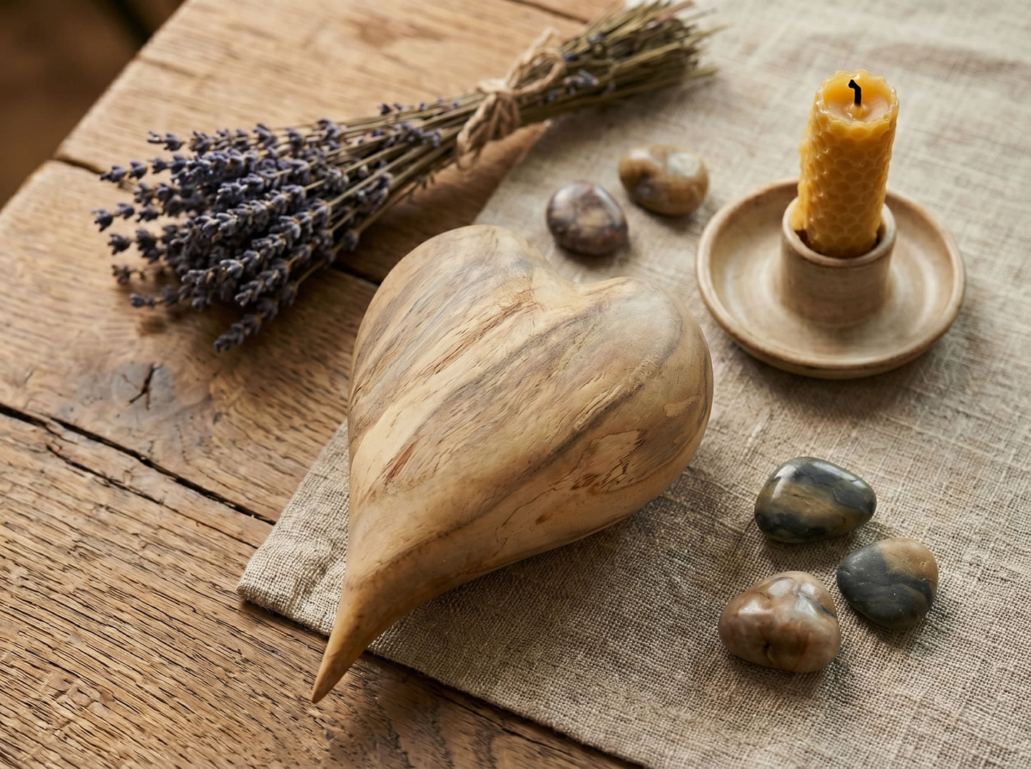 A carved timber heart with sweeping diagonal grain rests beside lavender and a beeswax candle.