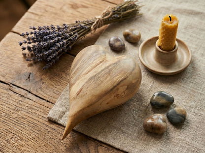 A carved timber heart with sweeping diagonal grain rests beside lavender and a beeswax candle.