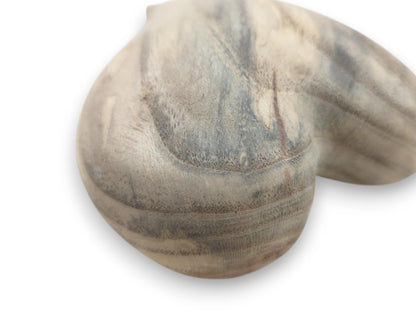 A close-up on a carved heart reveals porous end grain curving through marbled gray wood.