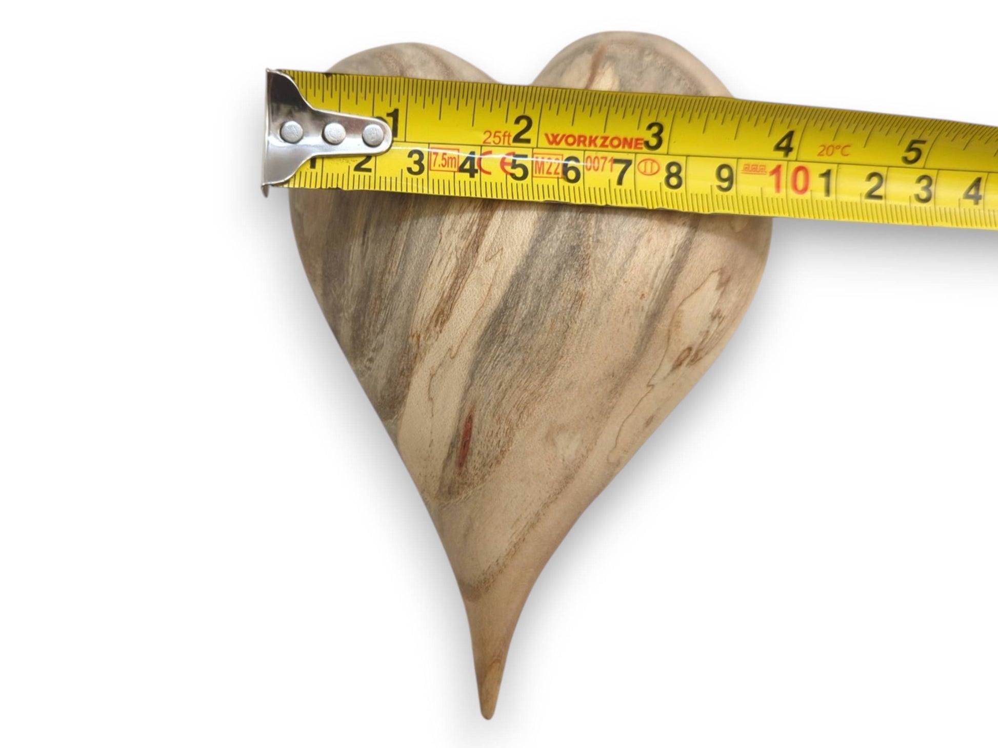 A yellow tape measure is laid across a wood heart, showing its four-inch width and striations.