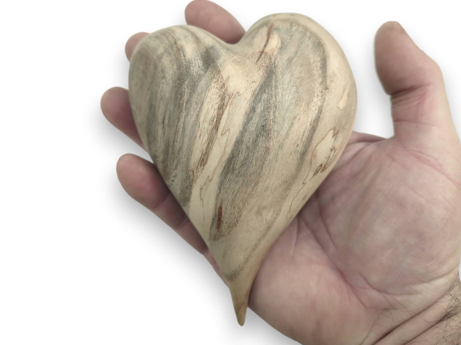 A palm cradles a carved heart showing dramatic gray mineral stains across its pale surface.