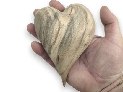 A palm cradles a carved heart showing dramatic gray mineral stains across its pale surface.