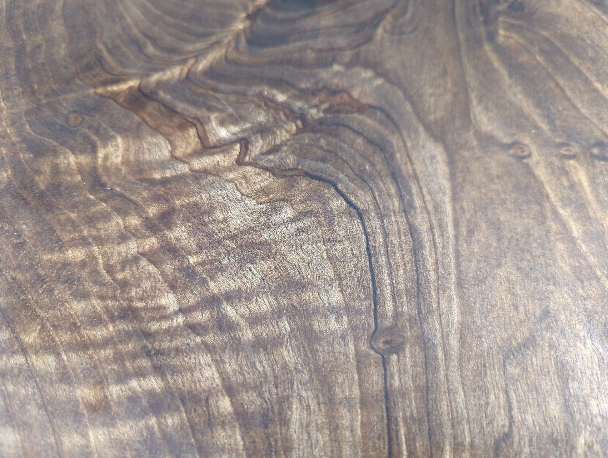 Detailed view of dark brown English walnut wood, showing intricate wavy grain, lighter tones, and small knots.