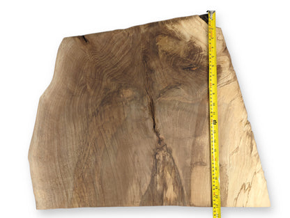 Live edge wood slab, varied brown with distinct swirling grain, measured by a yellow tape.