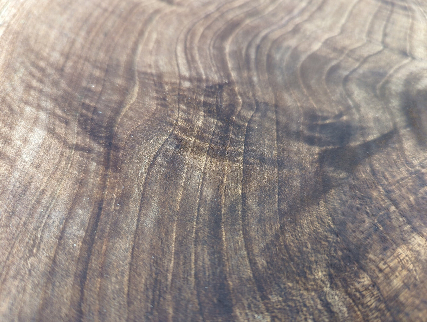 Detailed view of dark brown wood with prominent, wavy, lighter brown grain patterns and a smooth surface.