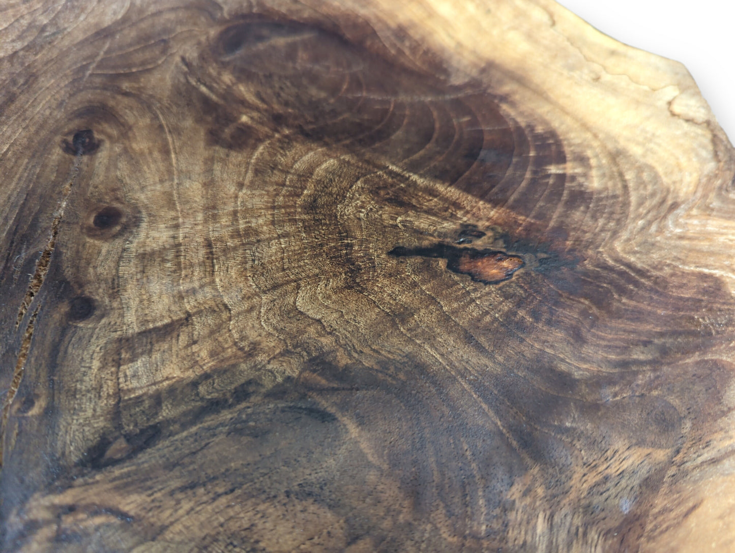 Varied dark brown wood surface exhibiting intricate, swirling grain patterns, darker knots, and smooth texture.