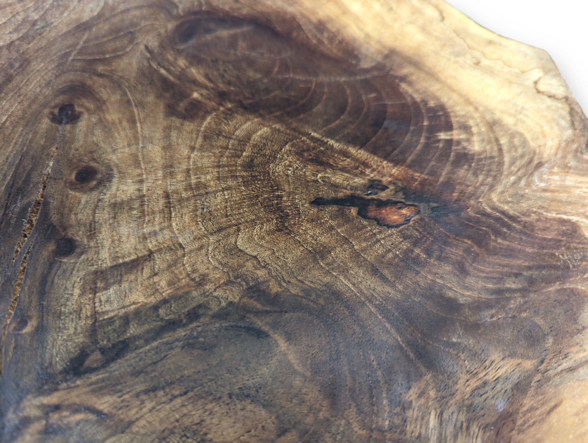 Varied dark brown wood surface exhibiting intricate, swirling grain patterns, darker knots, and smooth texture.