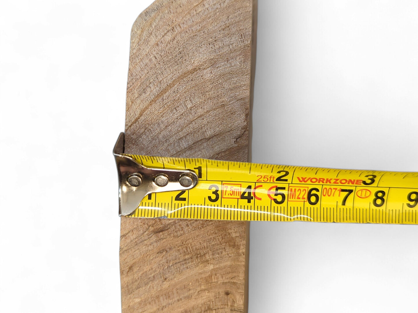 The thickness of a light brown wood slice, displaying visible grain, is measured by a yellow tape.