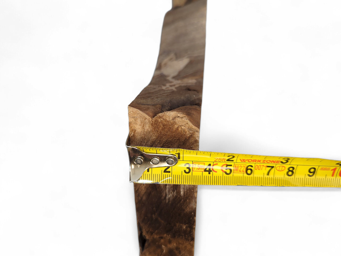 Rough-textured, dark brown wood slice edge measured by a yellow tape displaying inches and centimeters.