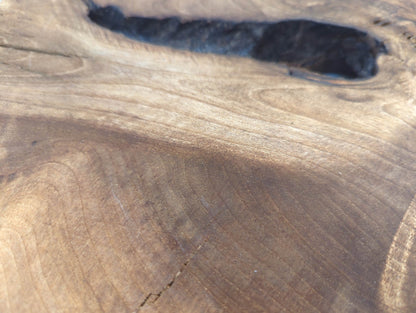 Brown walnut wood surface exhibits varied tones, prominent swirling grain, several natural fissures, and a large dark void.