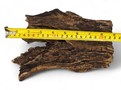 A yellow measuring tape is placed across a dark, deeply textured natural driftwood piece.