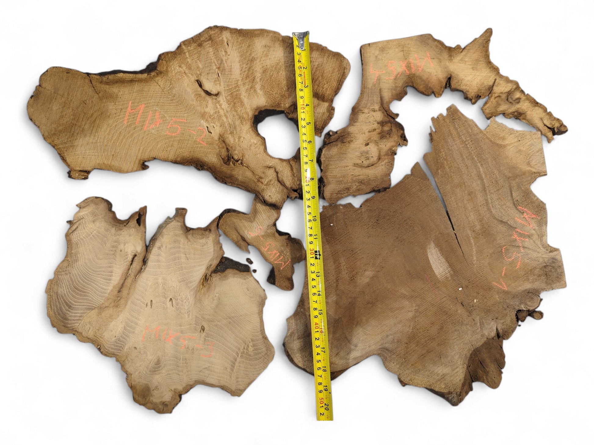Multiple irregular brown wood slices with prominent grain, dark live edges, and a yellow tape measure.