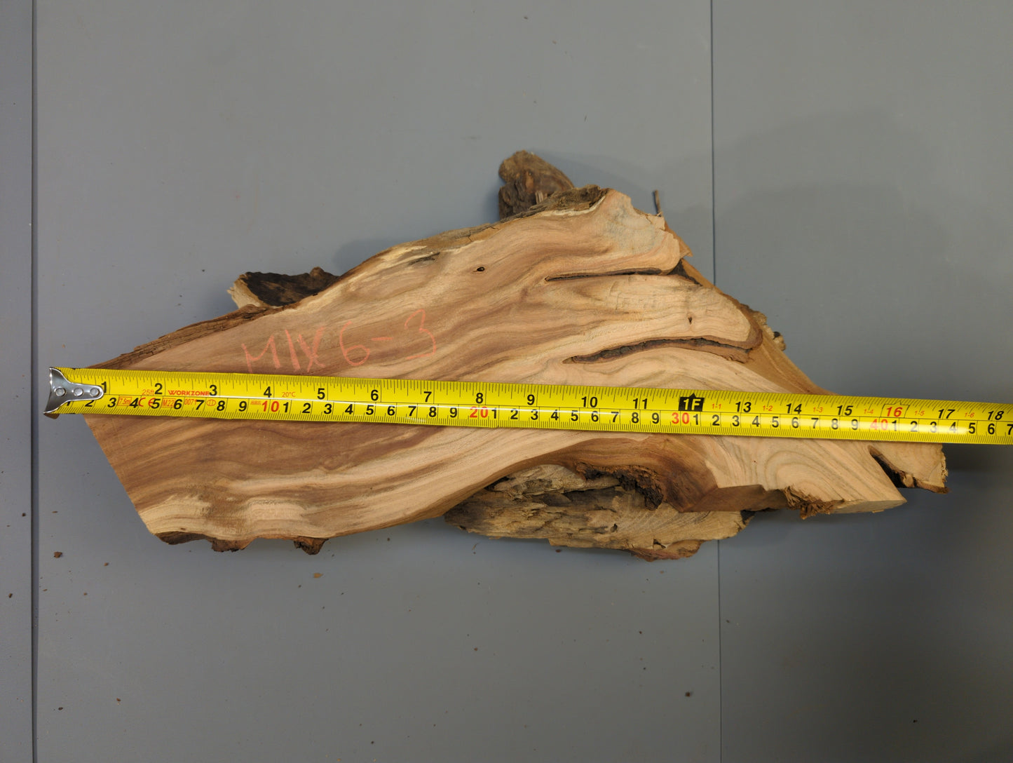 Irregular brown wood slice with live edge, prominent grain, red text, and a yellow measuring tape.