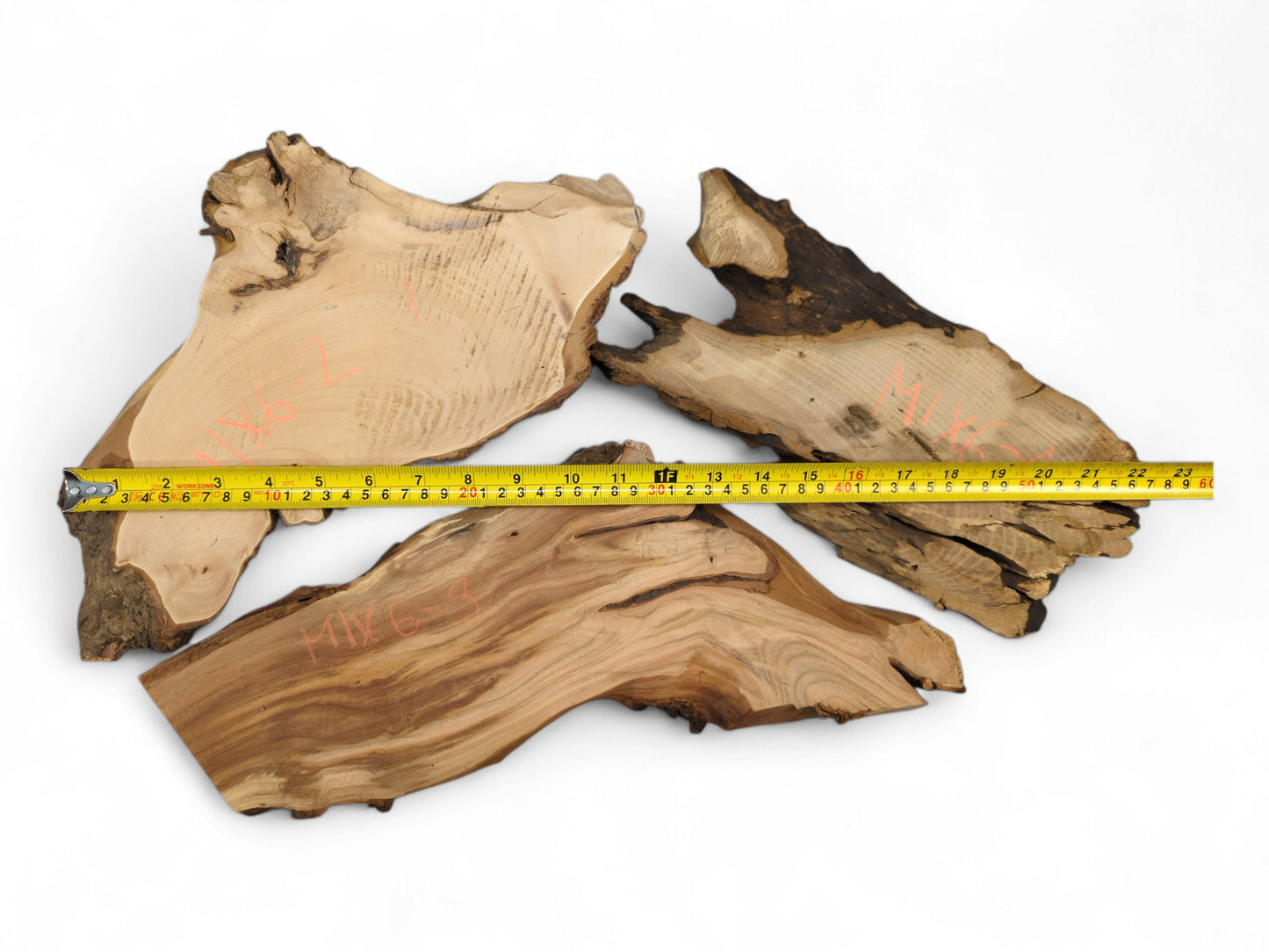 Multiple irregular wood slices, light brown with visible grain, dark live edges, and a measuring tape.