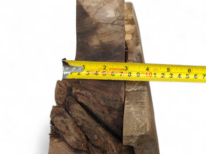 Yellow measuring tape indicates the five-inch width of a dark brown, textured, wedge-shaped wood slice.