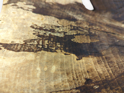 Close-up of a light brown wood surface, featuring dark, irregular patterns and distinct wood grain.