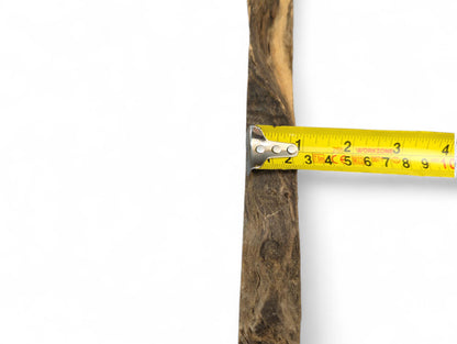 A long, narrow wood piece with dark and light brown grain, measured by a yellow tape.