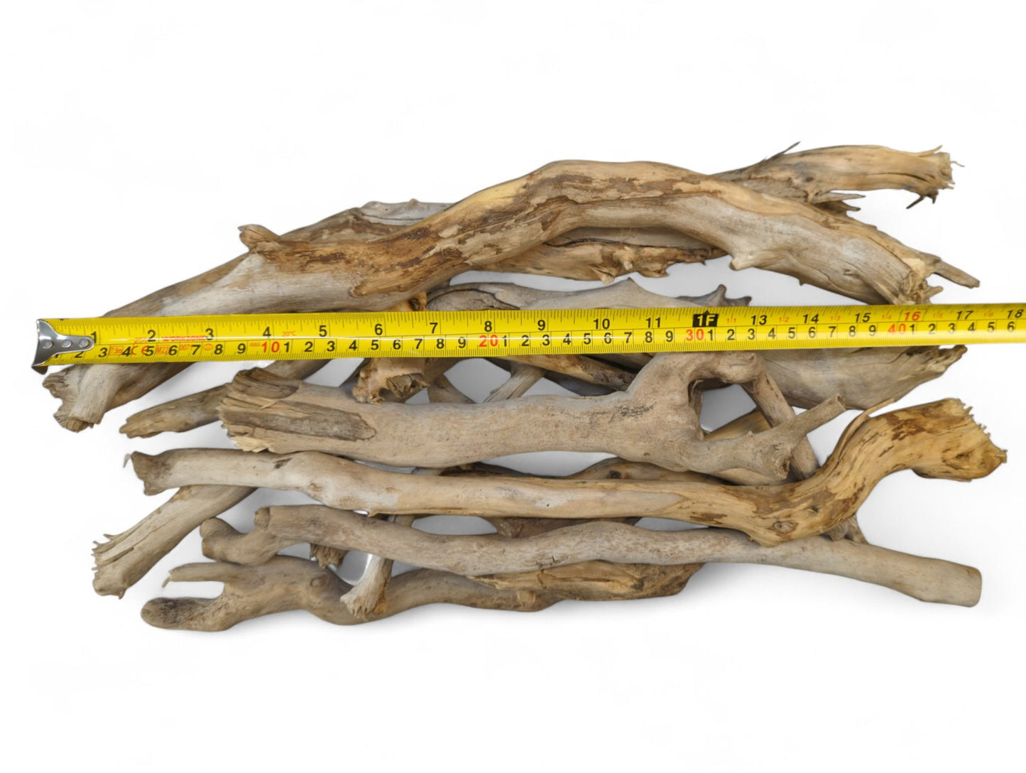 Pile of weathered, light brown and gray driftwood sticks measured by a yellow tape on white.