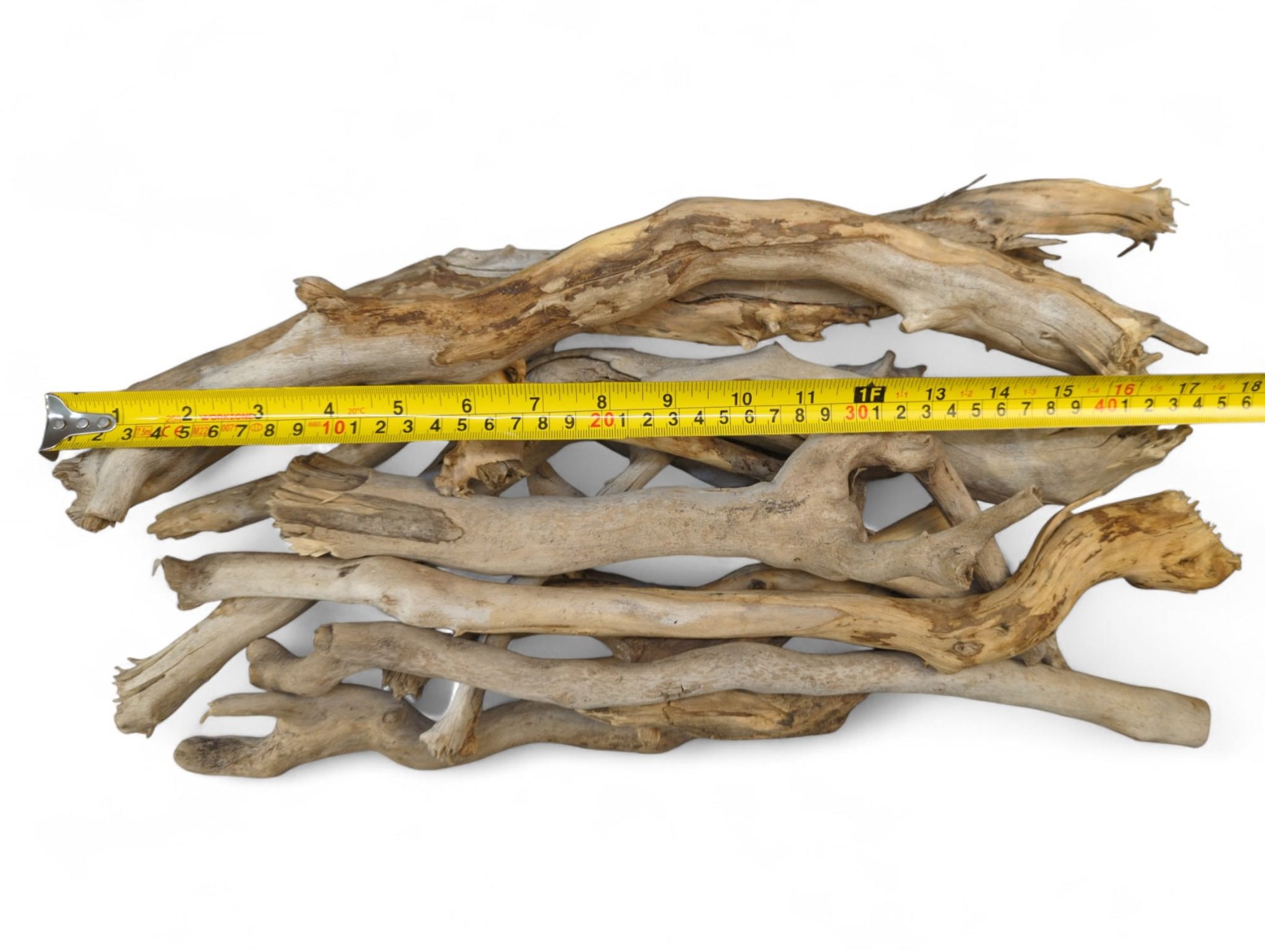 Pile of weathered, light brown and gray driftwood sticks measured by a yellow tape on white.